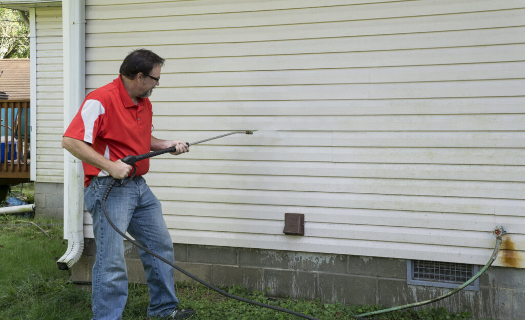 Contractor using a high pressure washer to remover algae and mold from a house with vinyl siding. Cleaning Siding