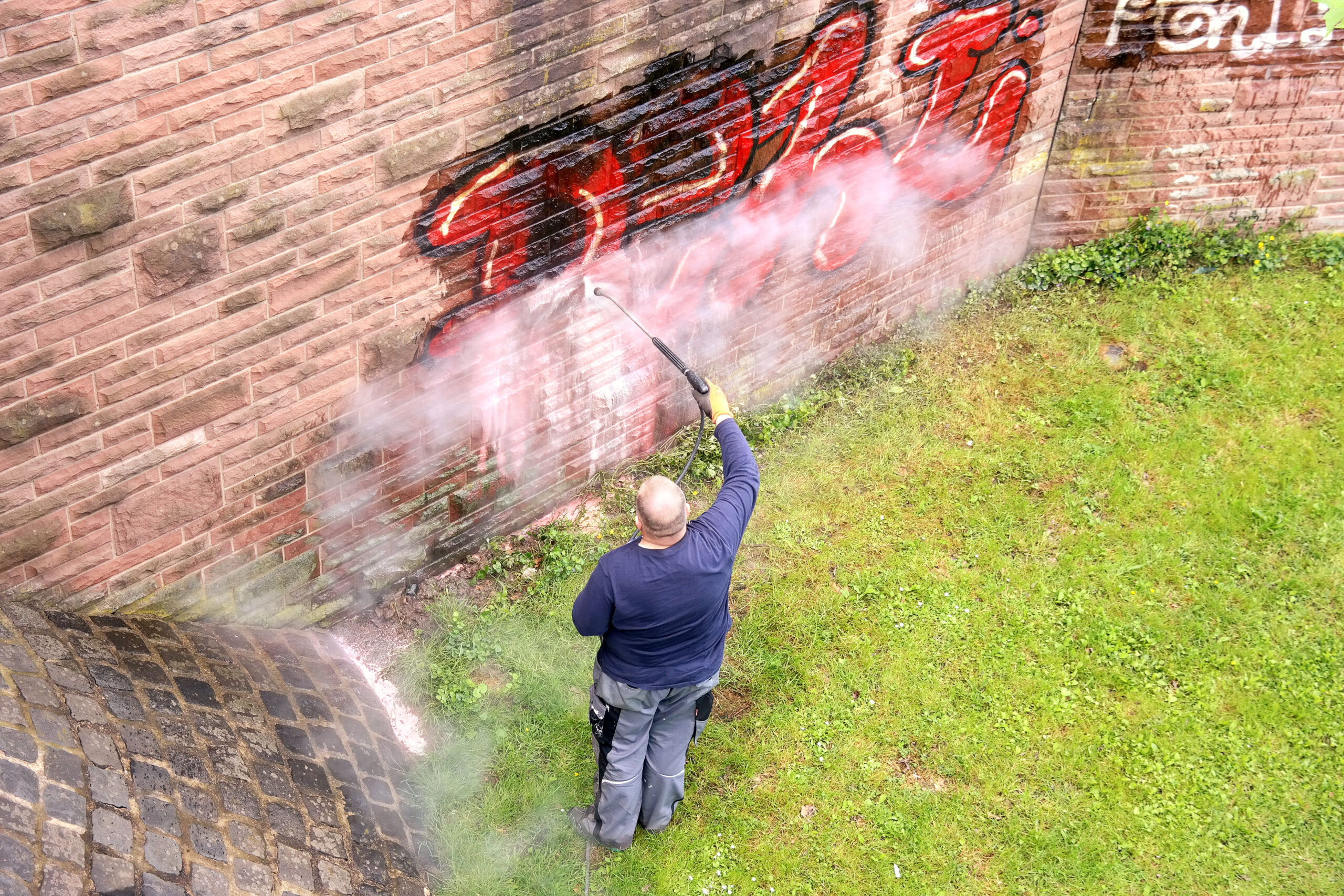 GERMANY, FRANKFURT AM MAIN - May 07.2014 : Worker of municipal service of city cleans a wall from graffiti. Remove Graffiti