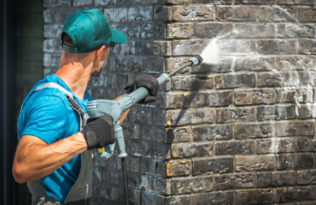 House Brick Wall Washing Using Pressure Washer. Caucasian Worker in His 30s. 
Pressure Wash Pollen